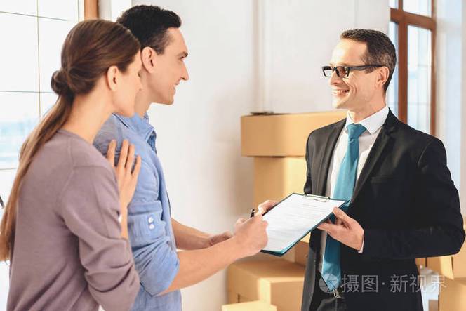 房地产经纪人与家庭在新的公寓与纸板箱.丈夫正在签合同